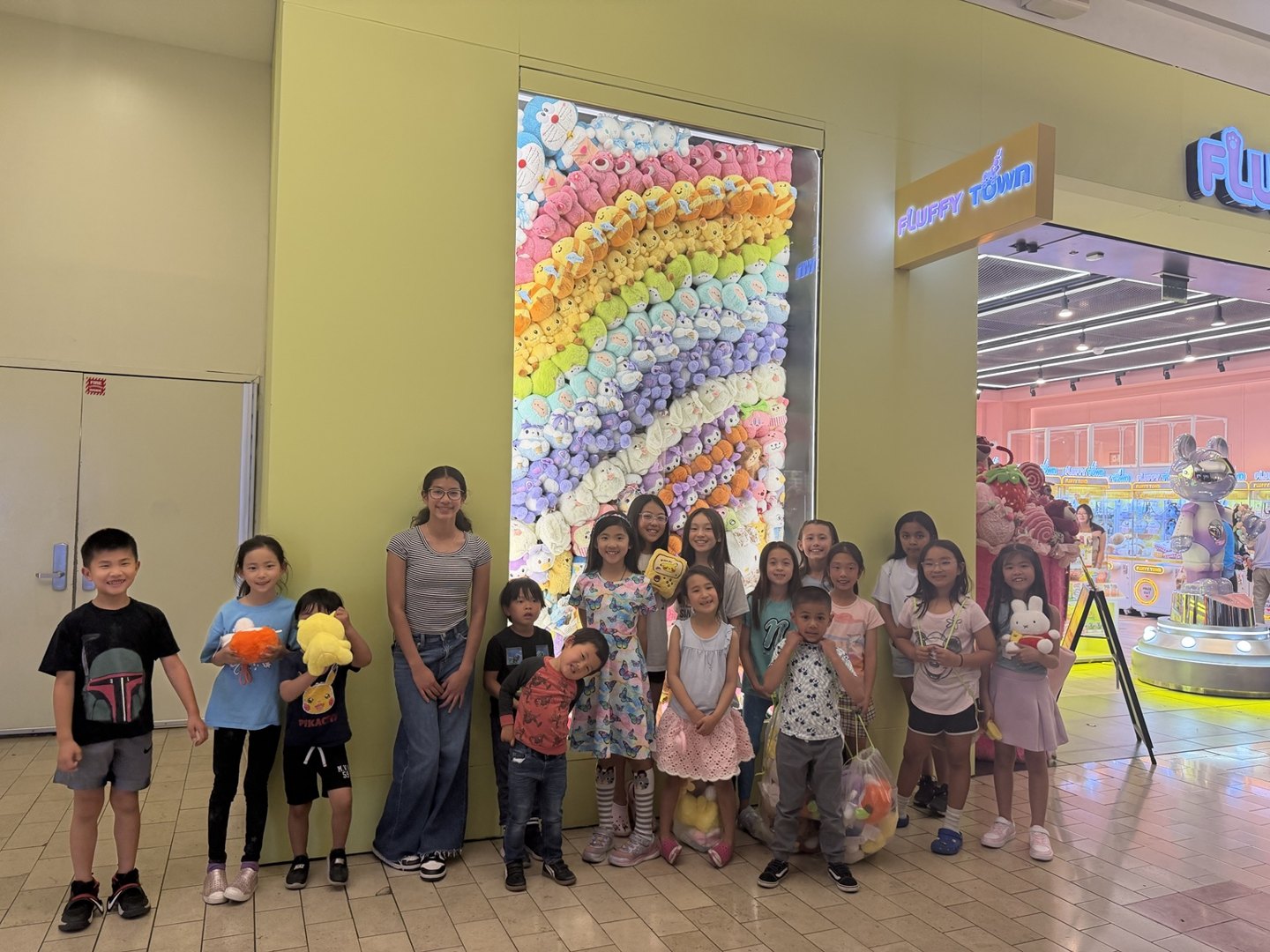 Birthday guests holding plush prizes in a group photo at the Rainbow Plush Wall