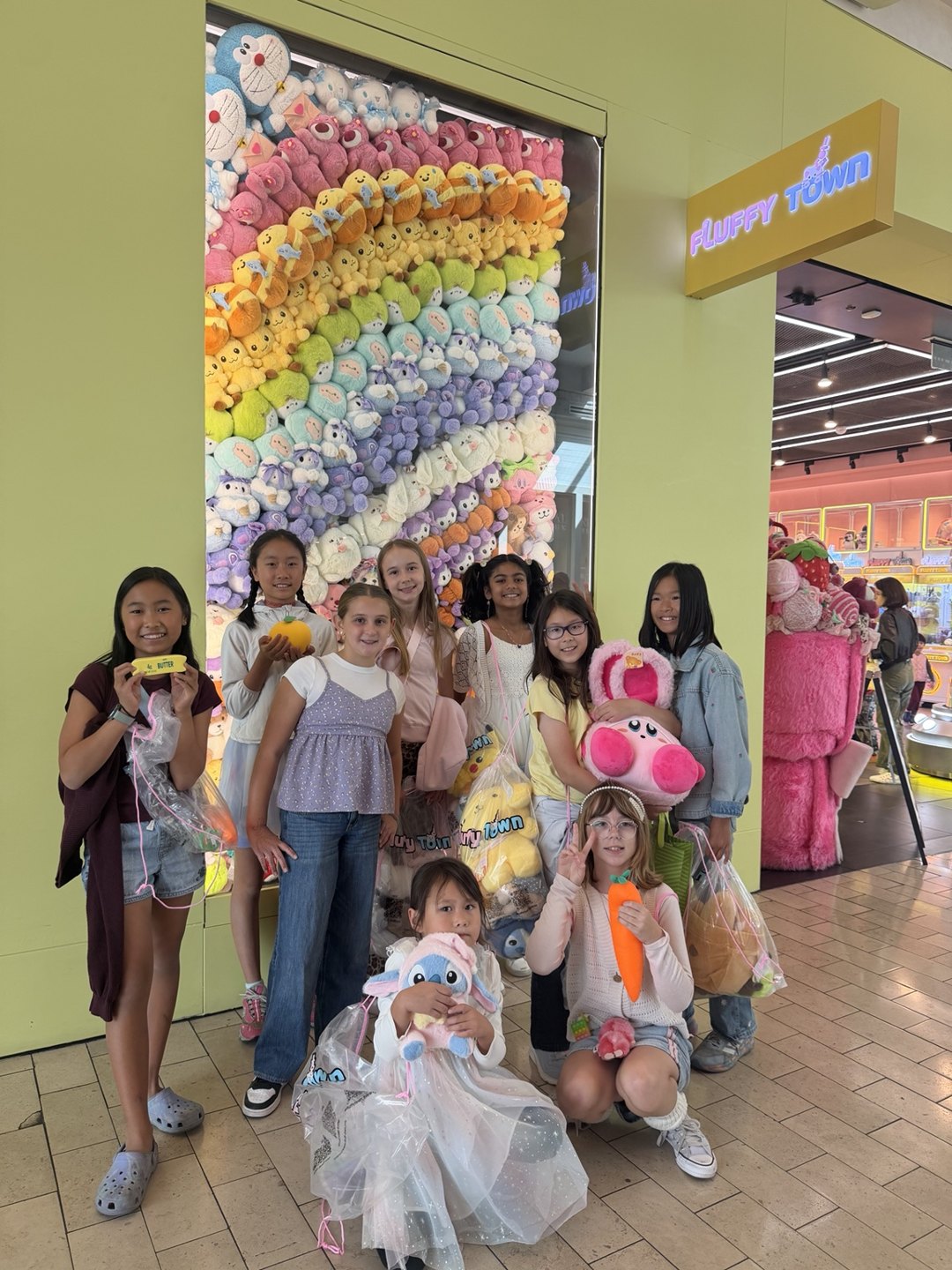 Birthday guests holding plush prizes together at Fluffy Town’s Rainbow Plush Wall